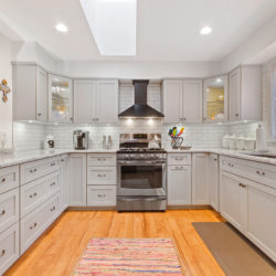 Off-white contemporary kitchen cabinets with white marble countertops, stainless steel appliances, and wall-mounted range hood, refaced kitchen cabinets in Williamsport, PA by Lowe’s National Refacing Systems.